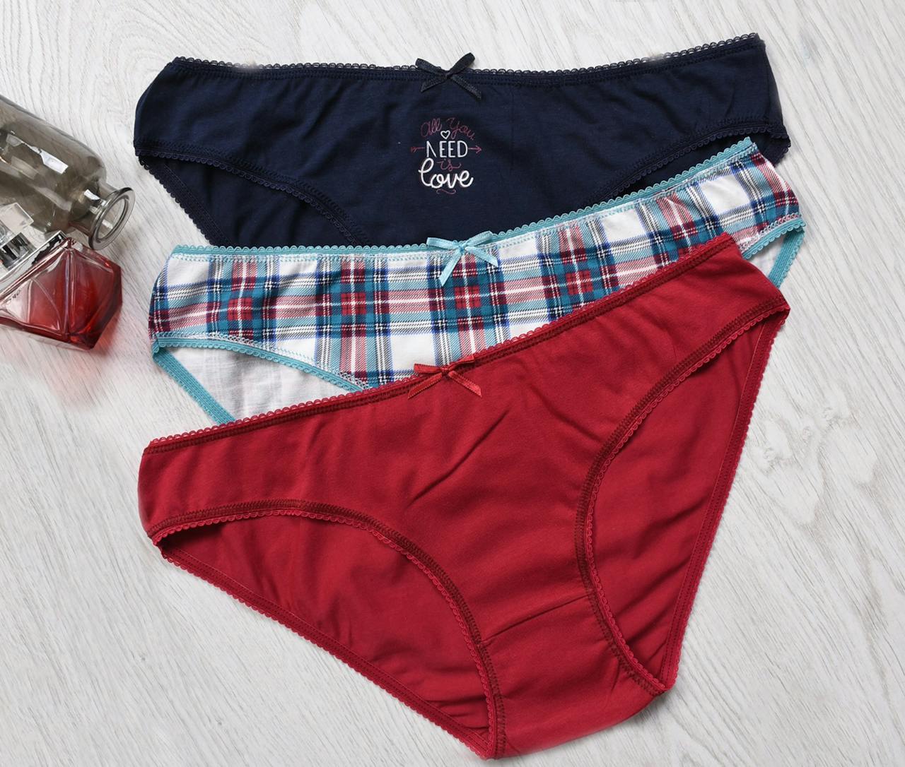 Three pairs of colorful women's underwear on a light wooden floor with a glass bottle.