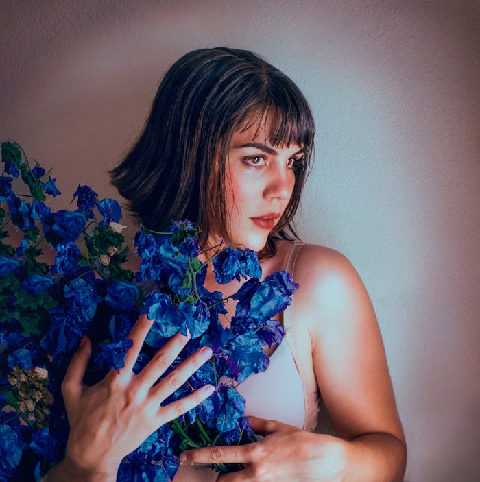 our-experience A young woman posing indoors with striking blue flowers, creating a modern and artistic vibe.
